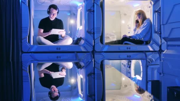 Молоді люди використовують гаджети, відпочиваючи в капсульному готелі — стокове відео