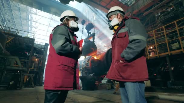 Metallurgiska fabriken med två industriarbetare som pratar. Metallurgisk fabriksinredning. — Stockvideo
