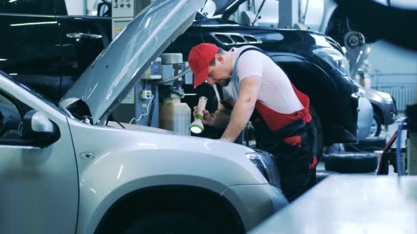 Automatisk mekaniker som använder ficklampa för att kontrollera insidan av en bil — Stockvideo