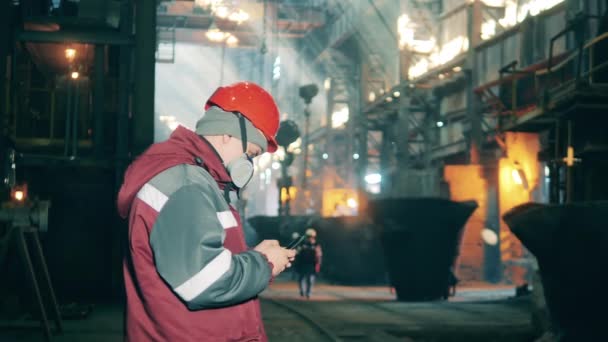 Steel worker with a mobile phone in the metallurgical plant. Metallurgical factory interior. — Stock Video