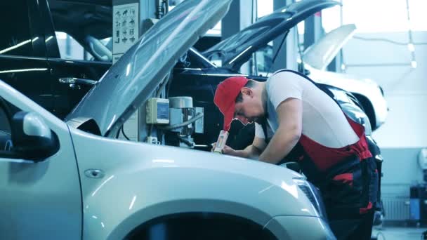 Carro mestre de reparação verifica sob o capô de um veículo com uma lanterna — Vídeo de Stock