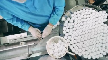 Fabrika işçisi, taşıyıcının ilaç tüplerini kapatıyor. İlaç fabrikası üretim hattı.
