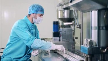 Erkek farmakolog konveyörde kapsül haplarını ayırıyor.
