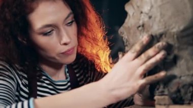 Bir kadın yüz hatları yaratmak için kilden bir heykeli yoğuruyor.