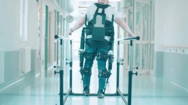 Hastane koridorunda, dış iskelette yürüme eğitimi almış bir adam var.