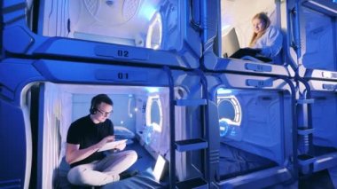 Genç bir adam ve bir kadın ayrı kapsül otel odalarında.