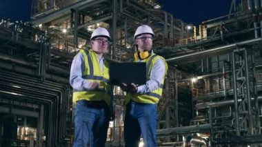 Petrol rafinerisinin içinde iki mühendis konuşuyor. Petrol endüstrisi, petrokimya fabrikası, rafineri konsepti.