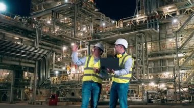 Dizüstü bilgisayarı olan iki mühendis petrol rafinerisinin içinde konuşuyorlar.