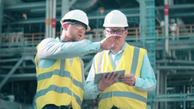 Petrol endüstrisi, petrokimya fabrikası, rafineri konsepti. Kask takan mühendisler petrol rafinerisinde konuşuyorlar.