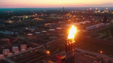 Petrol rafinerisinin gün batımı manzarası ve borular ateş saçıyor.