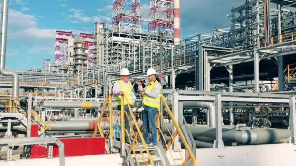 Oil refinery engineers are talking on the factory premises. Oil industry, petrochemical factory, refinery concept. — Stock Video