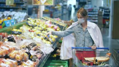 Yüzü maskeli bir kadının meyve alışverişi yaptığı bir süpermarket.