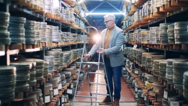 Archivar benutzt eine Leiter, um ein altes Filmband zu bekommen — Stockvideo