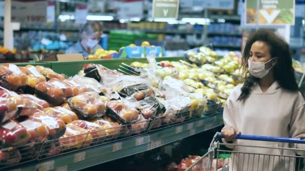 Une femme dans un masque facial choisit des fruits à acheter — Video