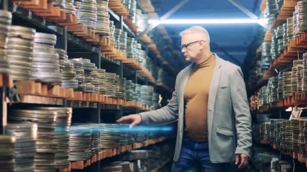 A man in glasses is walking through the movie archive. Retro, vintage technology concept. — Stock Video