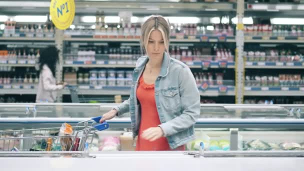 Un supermercado con una mujer recogiendo comida congelada. Mujer en un supermercado, concepto de consumismo. — Vídeos de Stock