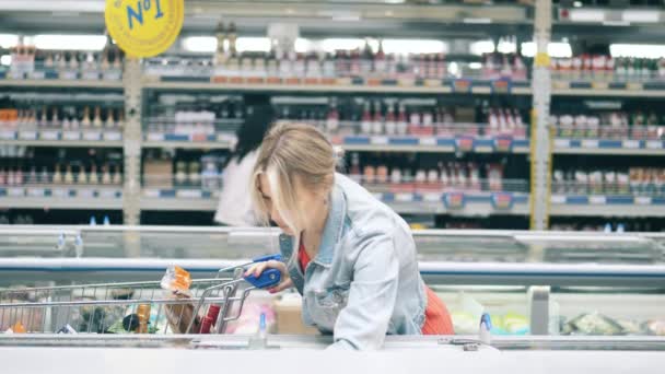 Mulher loira está escolhendo o que comprar no supermercado — Vídeo de Stock