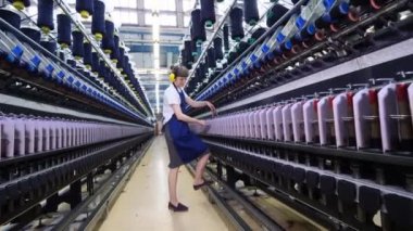 Kadın işçi fabrika makinelerindeki iplik makaralarını ayarlıyor.