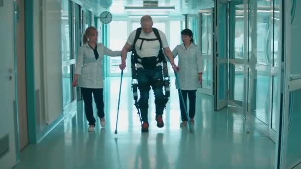 Artsen helpen een gehandicapte man om in het exosuit te lopen. — Stockvideo