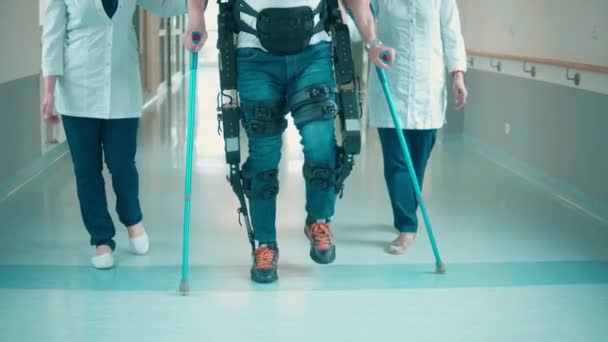 Homme patient dans l'exosquelette marche avec deux médecins — Video