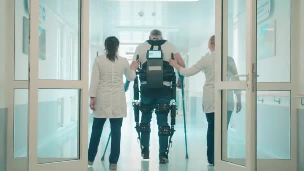 Doctors are helping male patient to walk in the exosuit — Stock Video