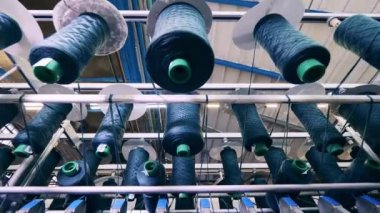 İplikli makaralar yavaş yavaş fabrika mekanizmasında dönüyor. Tekstil fabrikası üretim ekipmanları.