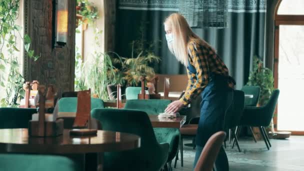 Blonde Kellnerin mit Mundschutz wischt den Tisch ab — Stockvideo