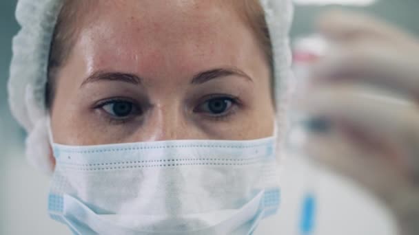Πρόσωπο γυναίκας γιατρού με μάσκα προσώπου που κοιτάζει το φάρμακο — Αρχείο Βίντεο