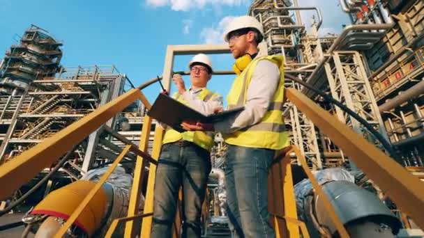 Planta de refinería de petróleo con dos trabajadores discutiendo un proyecto — Vídeos de Stock