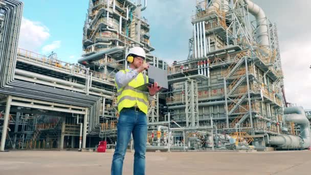 Ingeniero masculino está trabajando con un portátil cerca de la refinería de petróleo — Vídeos de Stock