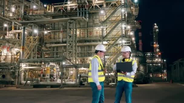 Los trabajadores están hablando en las instalaciones de la refinería de petróleo por la noche — Vídeos de Stock