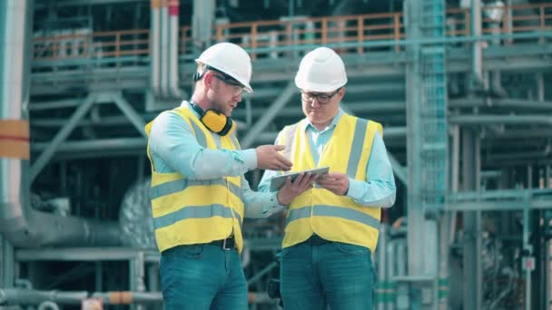 Engenheiros de refinaria de petróleo estão usando um tablet enquanto discutem planos — Vídeo de Stock