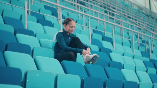 Jovem está amarrando os patins nos assentos da arena esportiva — Vídeo de Stock