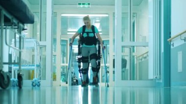 Dış iskeletteki engelli kadın koltuk değnekleriyle yürüyor.