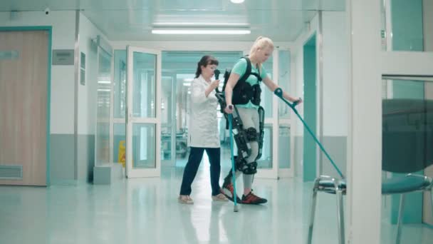 Doctor is helping a handicapped woman to move in the exosuit — Stock Video