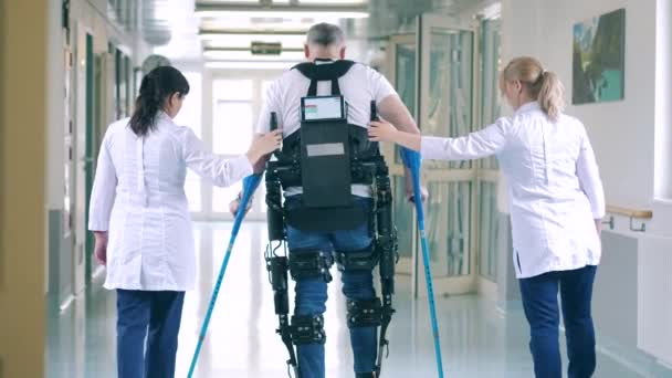 Las enfermeras están ayudando a un paciente discapacitado a caminar en el exosuit — Vídeo de stock