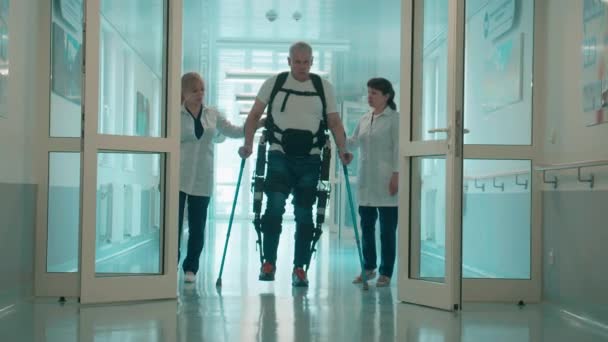 Un hombre en el exosuit está caminando con los médicos de ayuda — Vídeos de Stock