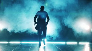 Bir oyuncu karanlık bir salonda basketbol topuyla numaralar yapıyor.