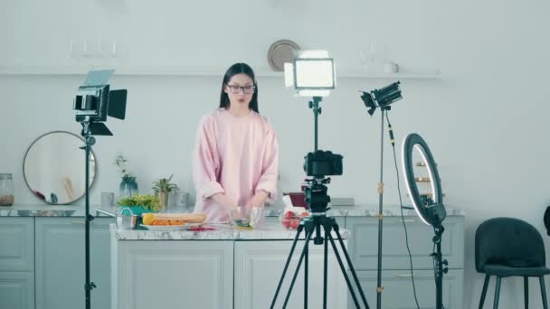 Jovem mulher alegre está cortando comida enquanto filma em um vlog — Vídeo de Stock