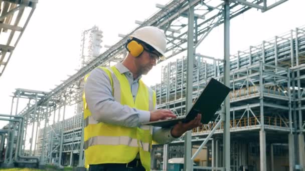 Raffinaderij werknemer met een laptop op het terrein van de fabriek — Stockvideo