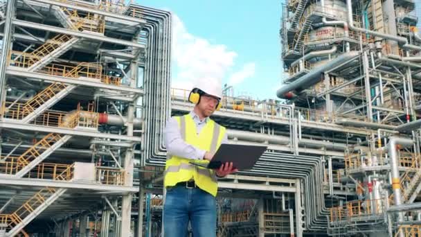 Raffinerie-Mitarbeiter in Sicherheitskleidung arbeitet mit Laptop im Freien — Stockvideo
