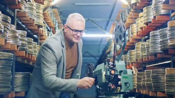 Experto en cine sonríe mientras regula proyector de cinta vintage — Vídeos de Stock