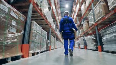 Yüz maskeli bir işçi depoda bir kutu taşıyor. Dış iskelet giyen mühendis, dış giysi.