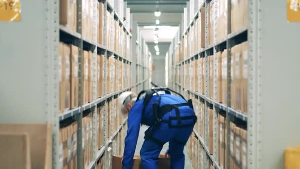 Warehouse worker in ergoskeleton is storaging a box into the shelf — Stock Video