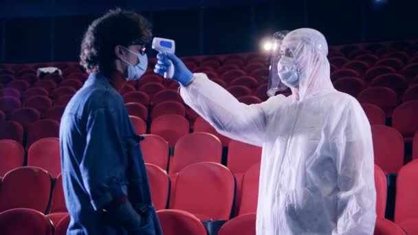 Man wearing a hazmat suit checks viewers temperature at the cinema — Stock Video