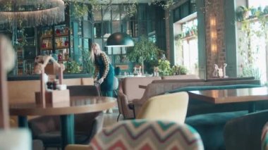 Neşeli garson restoranda masaları kontrol ediyor.