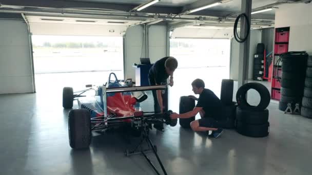 Dos hombres están arreglando las ruedas de un coche de carreras — Vídeos de Stock