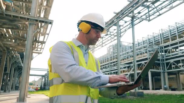 Trabajador industrial está operando una computadora portátil fuera de la refinería de petróleo — Vídeo de stock