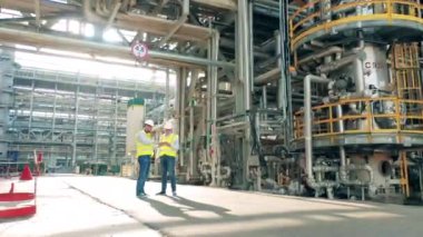 Rafineri mühendisleri fabrika borularının arasında konuşuyor.