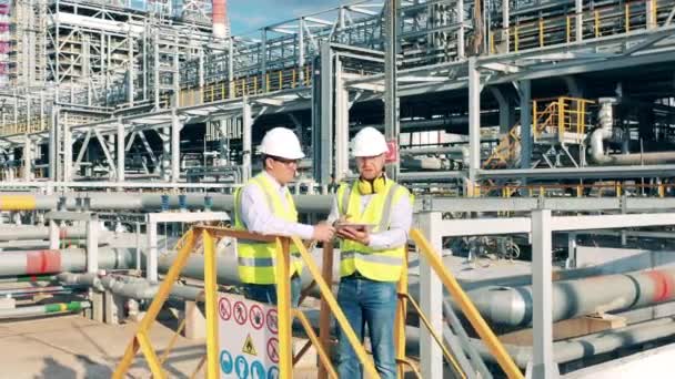 Trabalhadores industriais estão tendo uma conversa entre as construções da refinaria — Vídeo de Stock